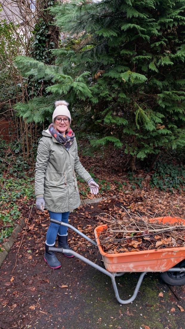 Roisin loading dead leaves into a wheelbarrow for composting